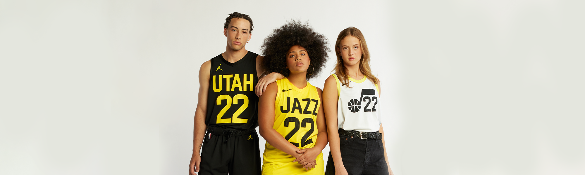 A Man and two women standing together, the man in the Black Jordan darkmode jersey, women in middle with the Yellow Nike Remix Jersey, and the other women wearing the white Nike association jersey