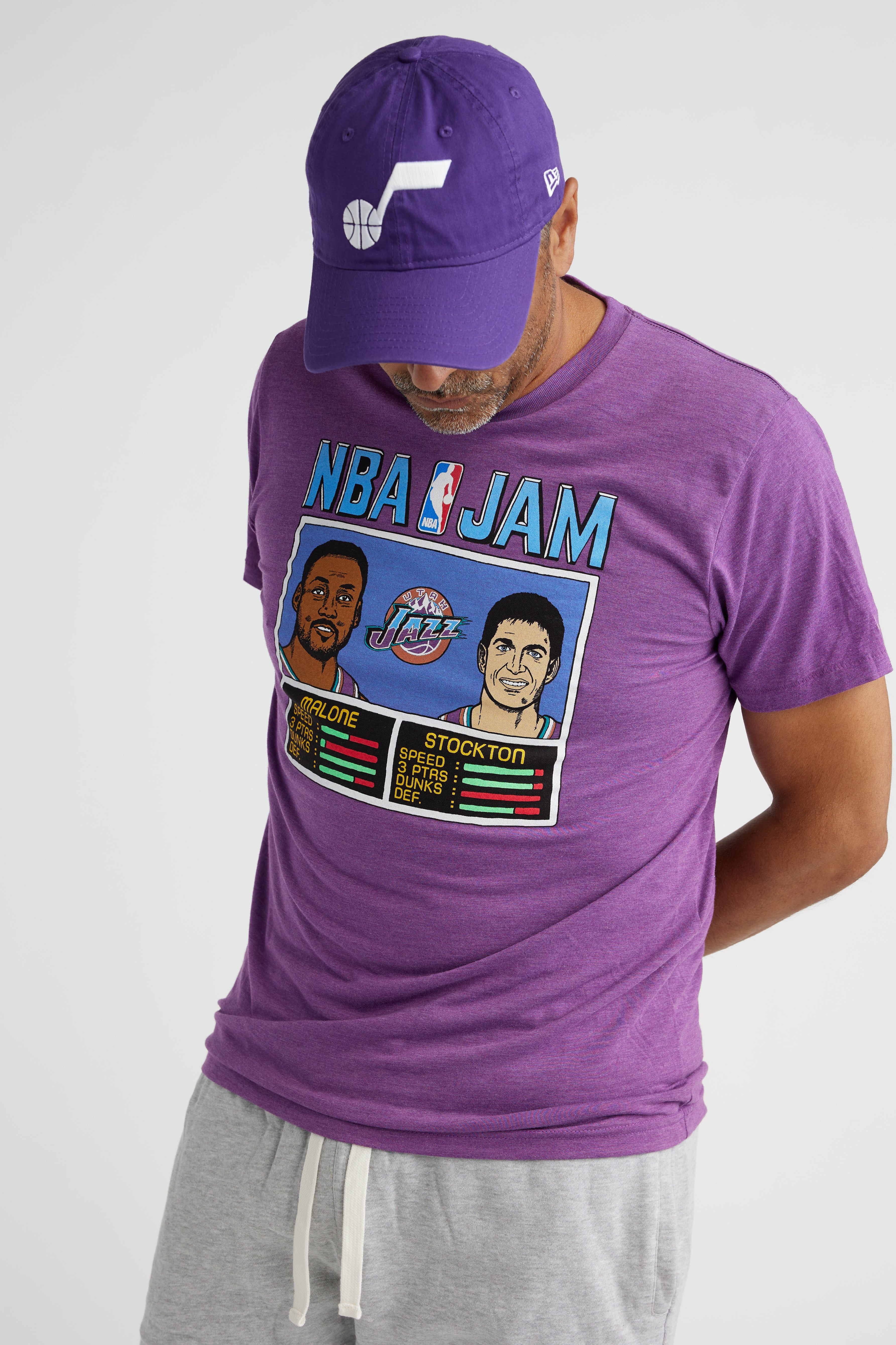 A man wearing the Purple NBA JAM homage tee featuring John Stockton and Karl Malone with their NBA JAm game stats below